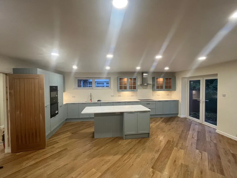 Sage-green kitchen with island, wooden floor and glazed doors