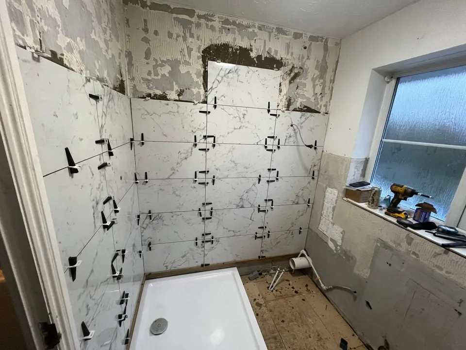 Wall tiles being set with levelling clips above the shower tray