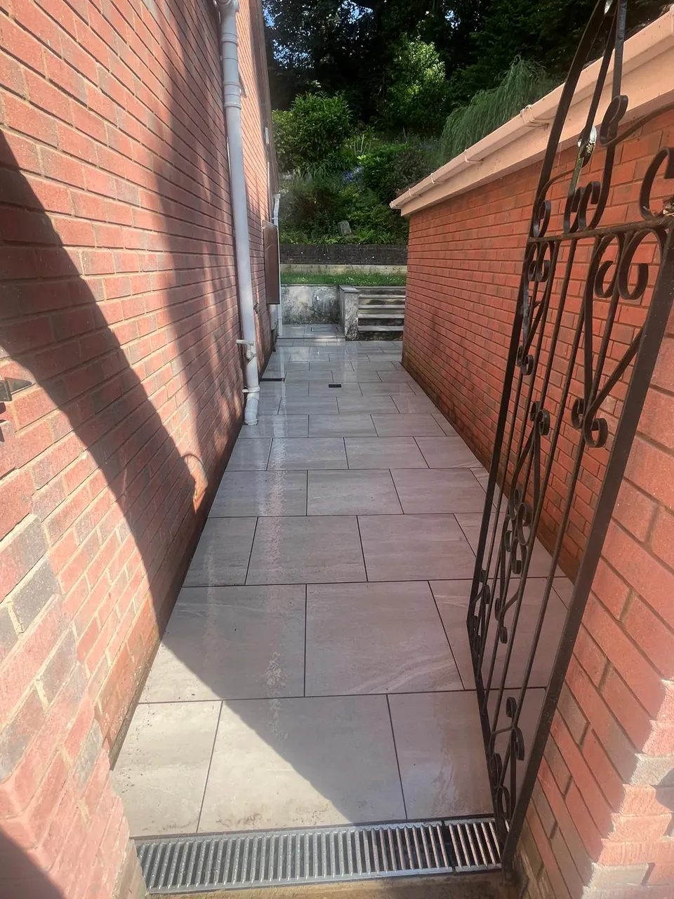 Grey porcelain paving along a brick side passage with a channel drain