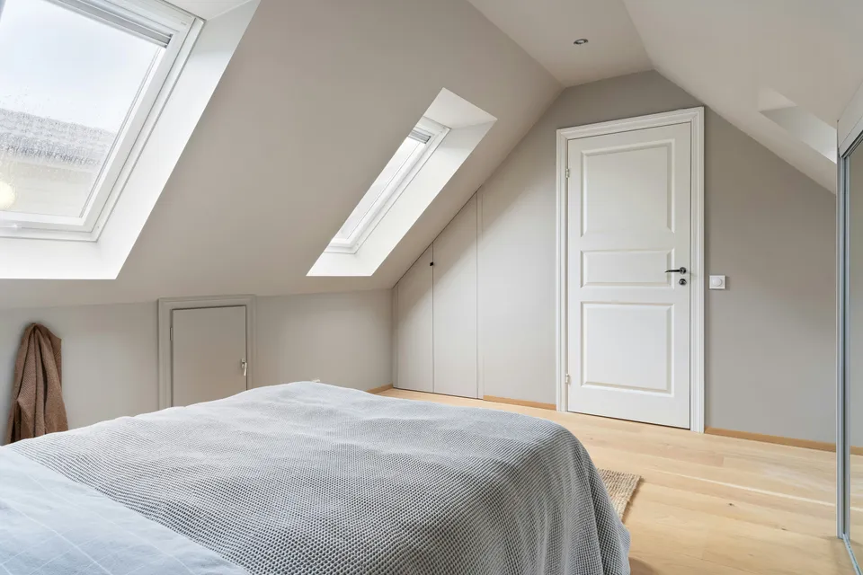 Bedroom under a sloping ceiling with two roof windows and built-in storage along the low wall