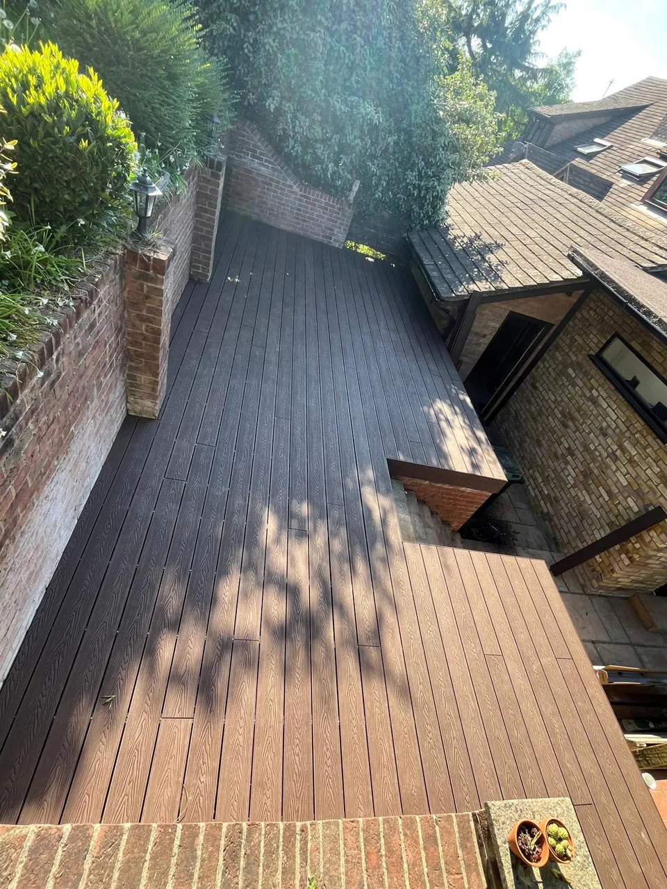 Brown composite decking on a raised terrace between a brick wall and the house