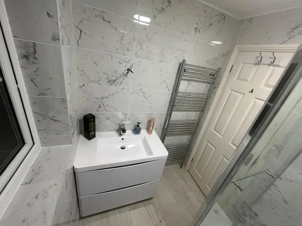 Basin vanity unit and heated towel rail with marble-effect wall tiles