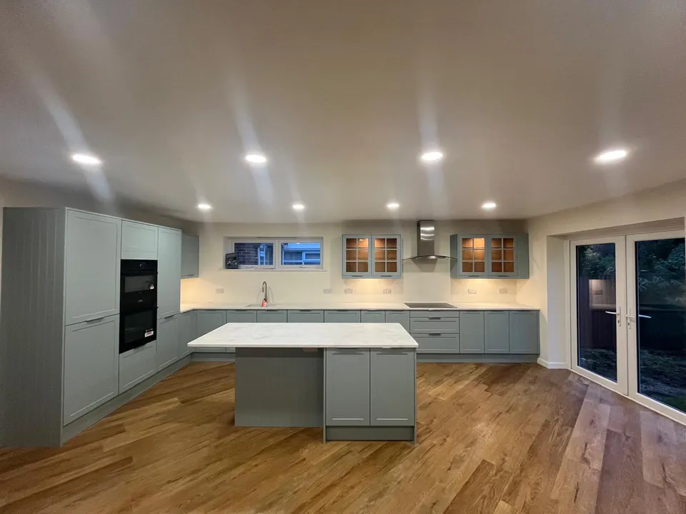 Sage-green kitchen units and island under recessed ceiling lights